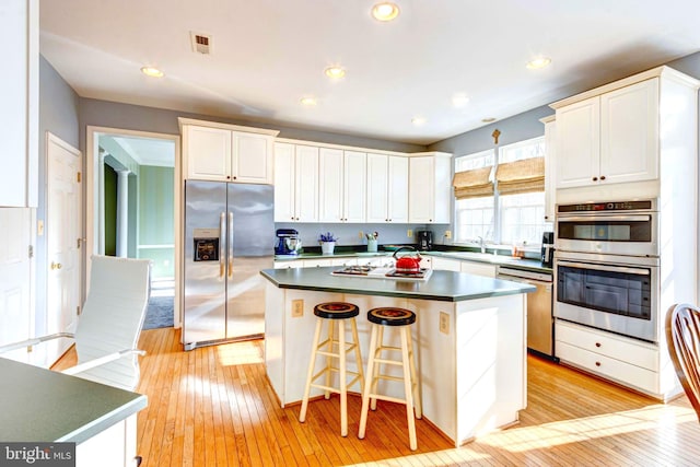 kitchen featuring a kitchen island, appliances with stainless steel finishes, a breakfast bar, white cabinets, and light hardwood / wood-style floors