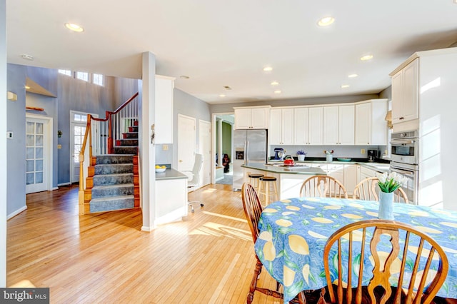 kitchen with stainless steel appliances, white cabinetry, a kitchen breakfast bar, and light wood-type flooring