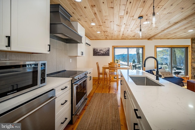 kitchen with hanging light fixtures, premium range hood, stainless steel appliances, sink, and white cabinetry