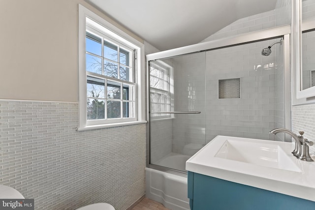 full bathroom featuring enclosed tub / shower combo, tile walls, vanity, and toilet