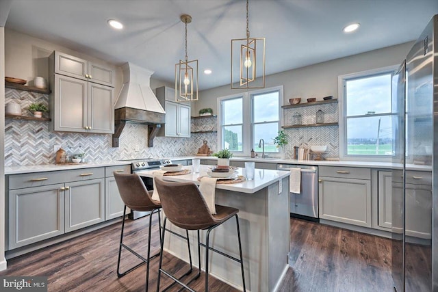 kitchen featuring pendant lighting, gray cabinets, appliances with stainless steel finishes, a center island, and custom range hood