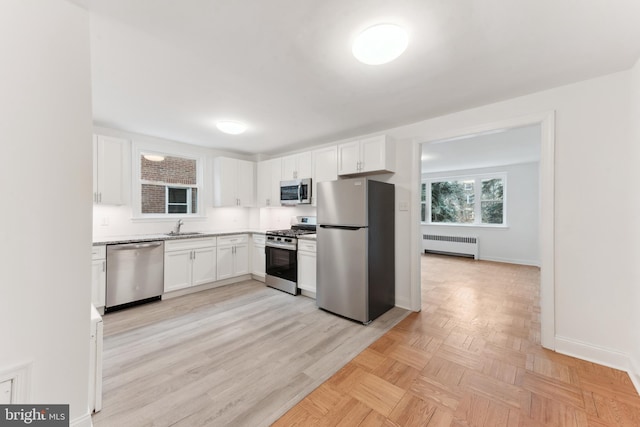 kitchen with radiator, stainless steel appliances, white cabinets, and sink