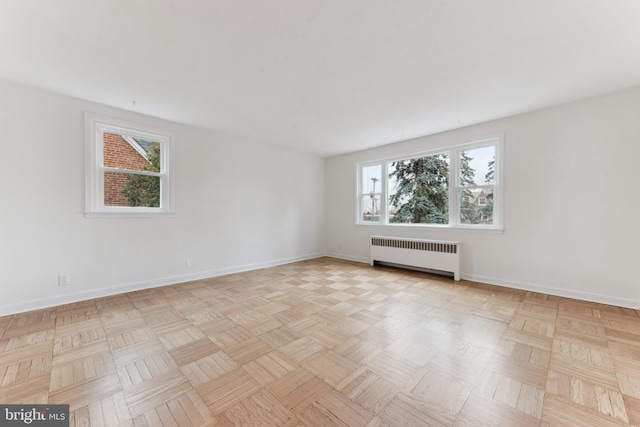 empty room featuring plenty of natural light, radiator heating unit, and light parquet flooring