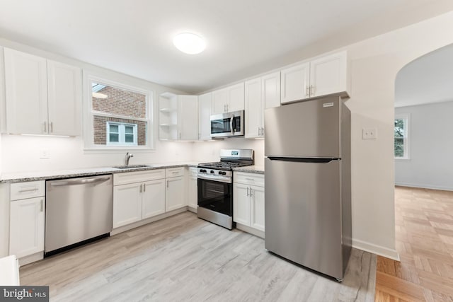 kitchen featuring white cabinetry, appliances with stainless steel finishes, light hardwood / wood-style flooring, light stone counters, and sink