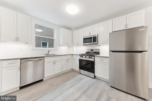 kitchen featuring sink, white cabinetry, light hardwood / wood-style flooring, light stone countertops, and appliances with stainless steel finishes