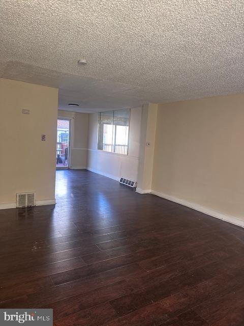 empty room with dark wood-type flooring and a textured ceiling