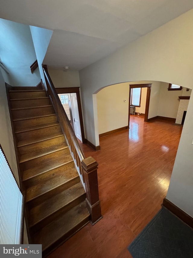 stairway with hardwood / wood-style floors, vaulted ceiling, and a brick fireplace