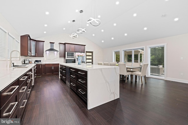 kitchen featuring lofted ceiling, built in microwave, hanging light fixtures, wall chimney range hood, and a center island