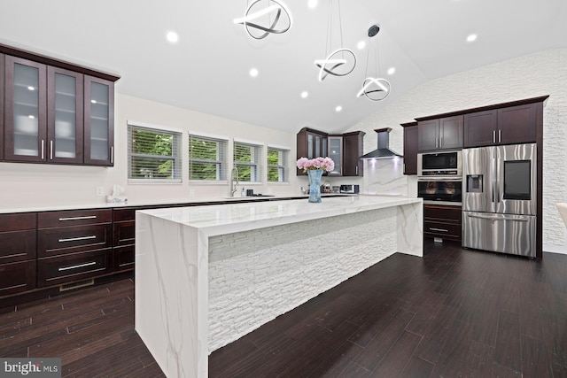 kitchen featuring a large island, stainless steel appliances, hanging light fixtures, vaulted ceiling, and wall chimney exhaust hood