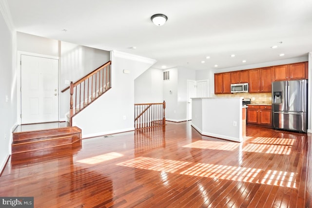 kitchen featuring stainless steel appliances, ornamental molding, hardwood / wood-style flooring, and backsplash