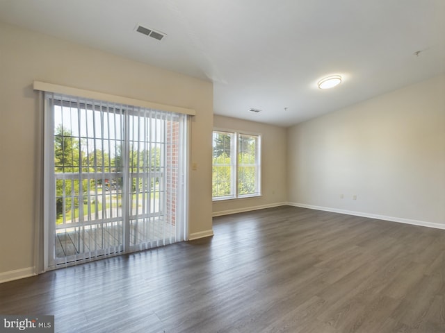 empty room with a wealth of natural light and dark hardwood / wood-style flooring