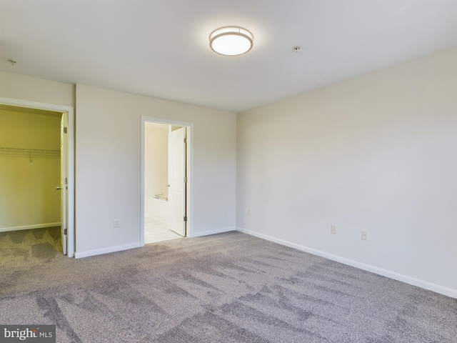 unfurnished bedroom with a spacious closet, ensuite bathroom, a closet, and carpet flooring