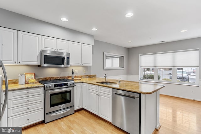 kitchen with kitchen peninsula, sink, light stone countertops, stainless steel appliances, and white cabinets