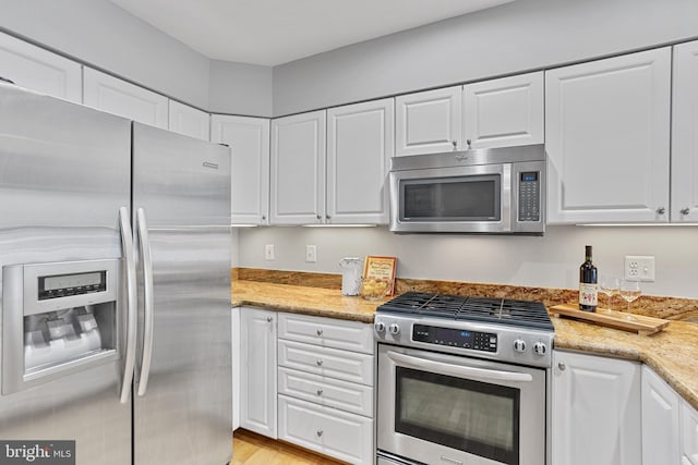 kitchen featuring appliances with stainless steel finishes, light hardwood / wood-style floors, white cabinetry, and light stone counters