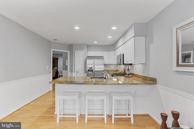 kitchen with white cabinets, stainless steel appliances, sink, kitchen peninsula, and a breakfast bar