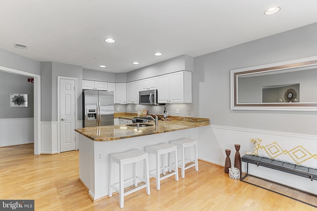 kitchen with kitchen peninsula, appliances with stainless steel finishes, white cabinets, and sink