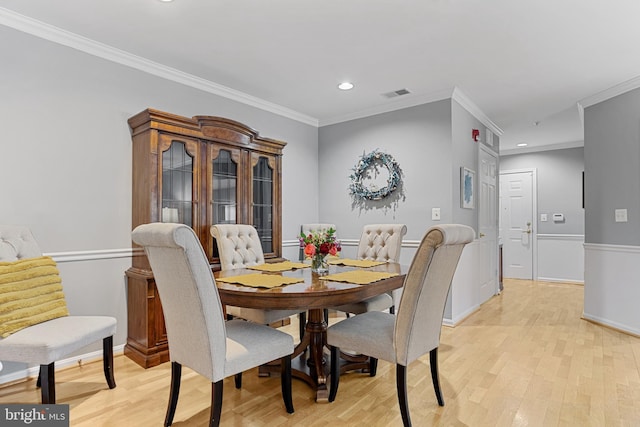 dining space with ornamental molding and light hardwood / wood-style flooring