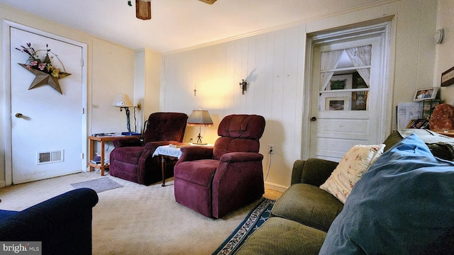 carpeted living room featuring ceiling fan, crown molding, and wood walls