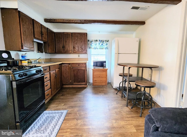 kitchen featuring white refrigerator, black range with gas stovetop, beamed ceiling, and light wood-type flooring