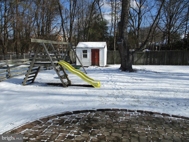 yard covered in snow featuring a playground and a storage shed