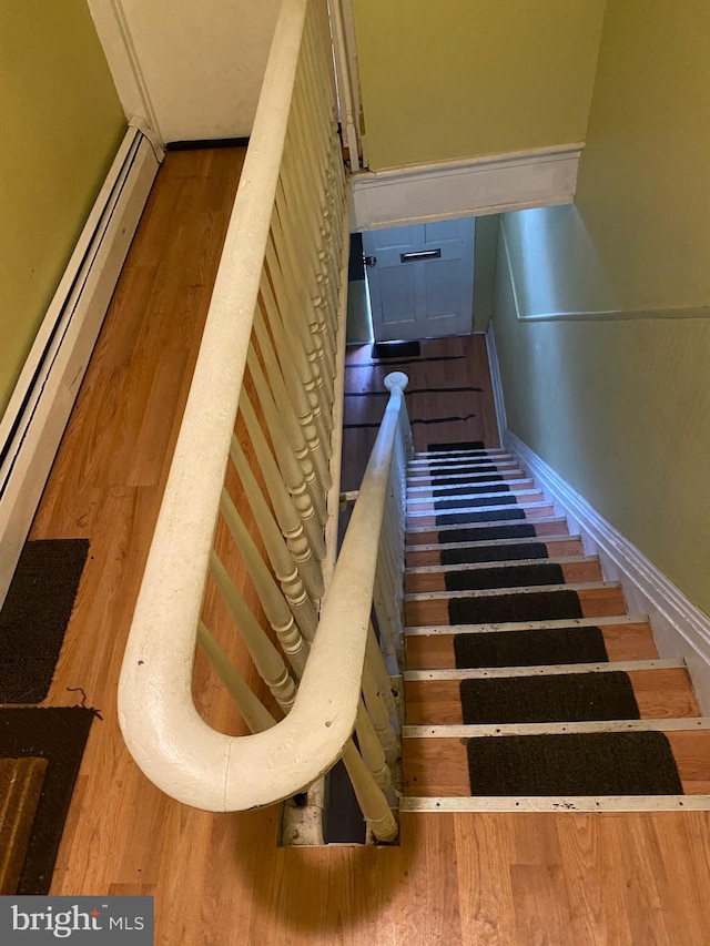 staircase with baseboard heating and hardwood / wood-style floors