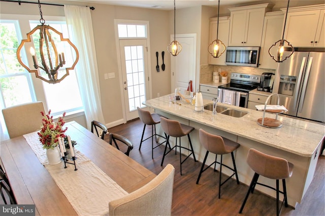 kitchen featuring a center island with sink, a breakfast bar, hanging light fixtures, light stone countertops, and stainless steel appliances