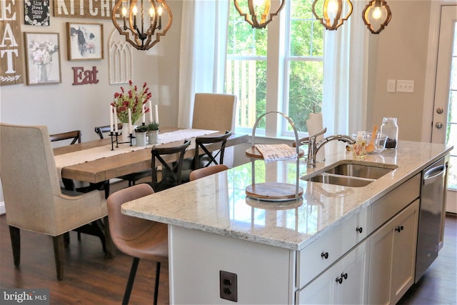 kitchen featuring light stone countertops, sink, pendant lighting, and an island with sink