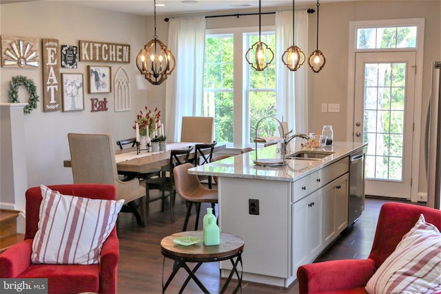 kitchen featuring decorative light fixtures, light stone countertops, stainless steel dishwasher, and a center island with sink