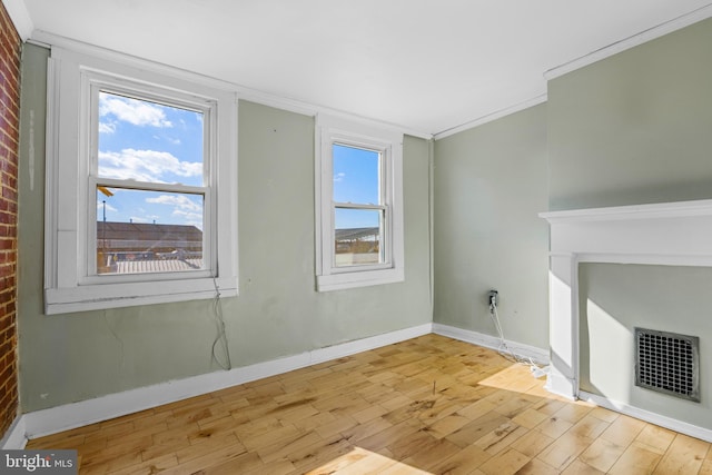 unfurnished living room featuring light wood-type flooring, ornamental molding, a fireplace, and a healthy amount of sunlight