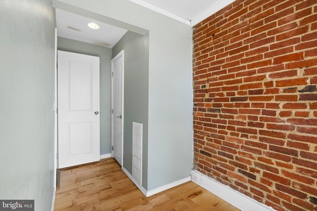 hallway with crown molding, brick wall, and light hardwood / wood-style flooring