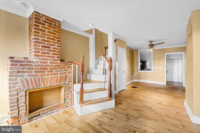 stairs with a fireplace, crown molding, ceiling fan, and wood-type flooring