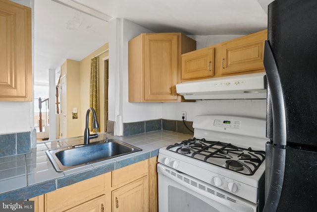 kitchen featuring white gas range, tile countertops, black refrigerator, sink, and light brown cabinets