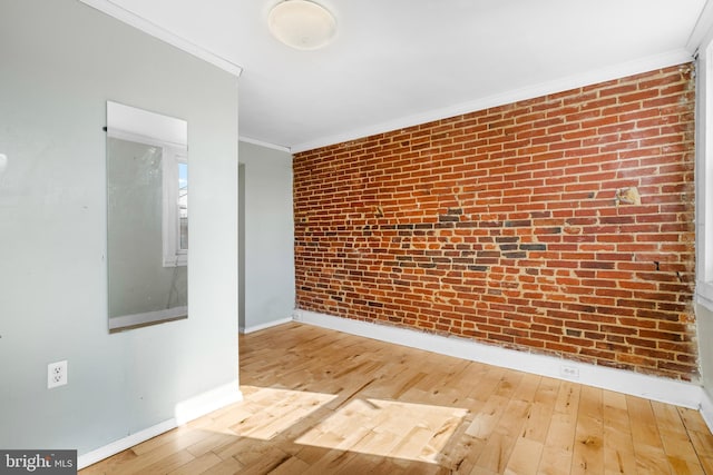 unfurnished room featuring hardwood / wood-style floors, brick wall, and ornamental molding