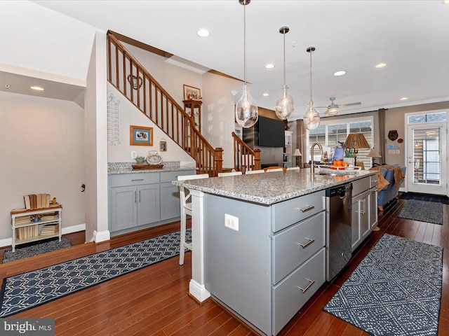 kitchen with stainless steel dishwasher, dark hardwood / wood-style flooring, hanging light fixtures, and a center island with sink