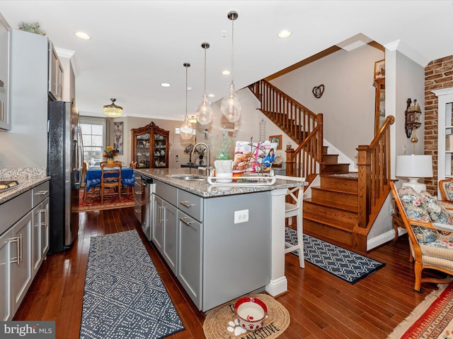 kitchen with gray cabinets, decorative light fixtures, a kitchen island with sink, stainless steel appliances, and light stone countertops