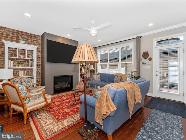 living room with dark wood-type flooring, ornamental molding, ceiling fan, and brick wall