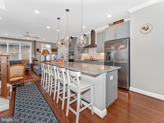 kitchen featuring light stone counters, hanging light fixtures, appliances with stainless steel finishes, gray cabinets, and wall chimney range hood