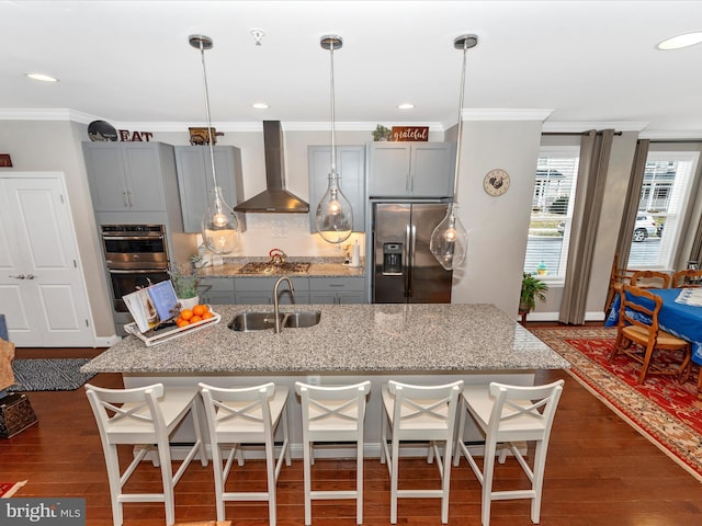 kitchen with hanging light fixtures, appliances with stainless steel finishes, wall chimney range hood, and a kitchen bar