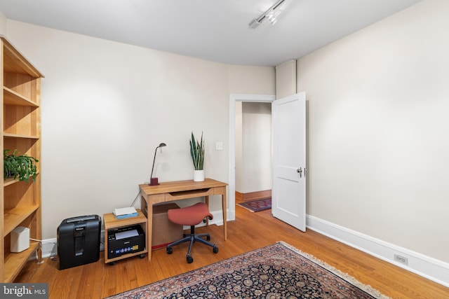 office with light hardwood / wood-style floors and rail lighting