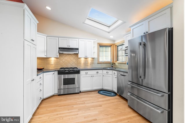 kitchen featuring appliances with stainless steel finishes, vaulted ceiling with skylight, sink, white cabinets, and backsplash