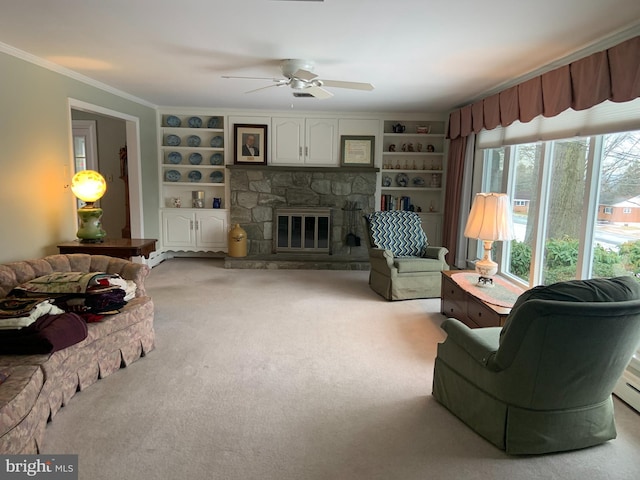 carpeted living room with ceiling fan, built in shelves, crown molding, and a stone fireplace