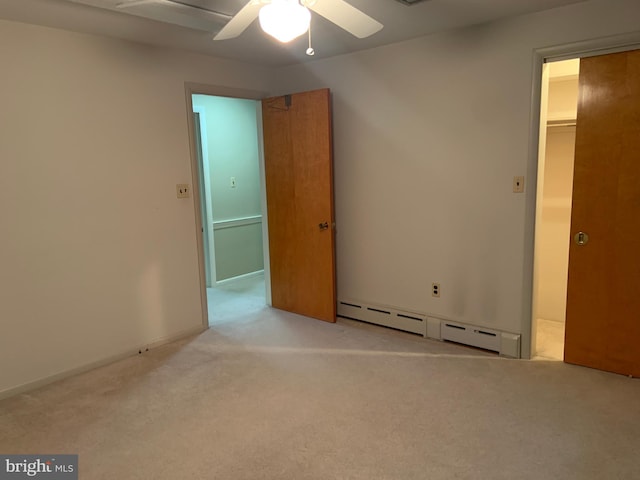 unfurnished bedroom featuring ceiling fan, light colored carpet, a baseboard heating unit, a walk in closet, and a closet