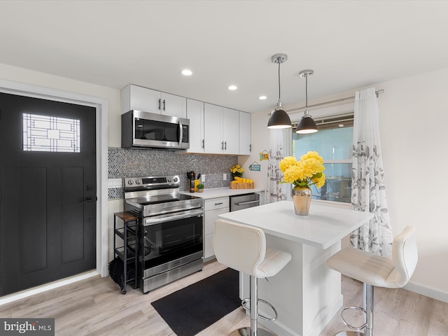 kitchen featuring appliances with stainless steel finishes, backsplash, pendant lighting, white cabinets, and a breakfast bar