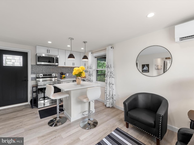 kitchen featuring decorative light fixtures, a wall unit AC, a breakfast bar, white cabinetry, and stainless steel appliances