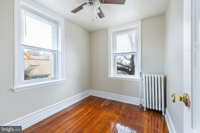 unfurnished room featuring a healthy amount of sunlight, radiator, ceiling fan, and dark hardwood / wood-style flooring