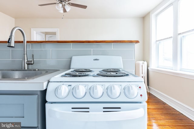 kitchen featuring sink, light wood-type flooring, radiator, white range with electric cooktop, and backsplash