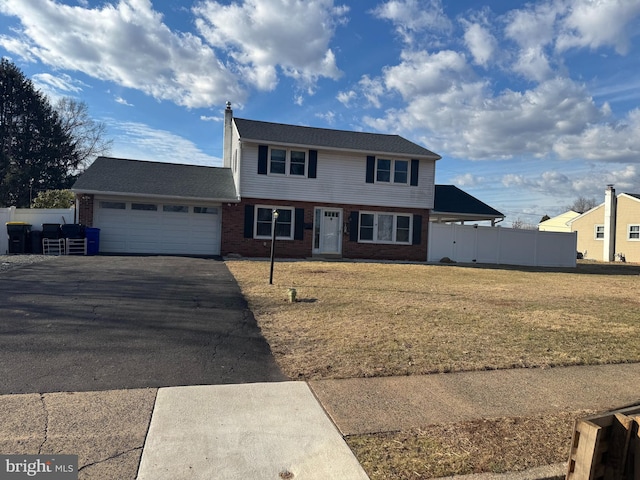 colonial home featuring aphalt driveway, a garage, brick siding, fence, and a front yard