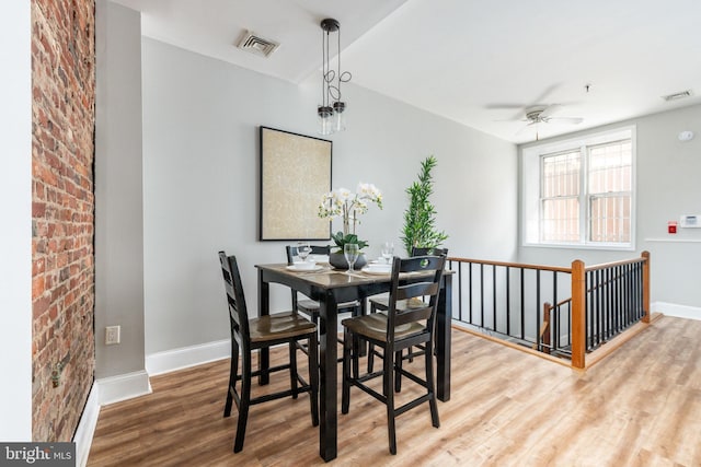 dining area featuring ceiling fan, brick wall, and wood-type flooring