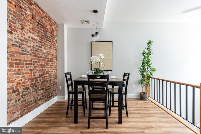 dining area with wood-type flooring and brick wall