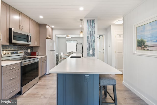 kitchen with sink, light wood-type flooring, pendant lighting, stainless steel appliances, and a kitchen island with sink